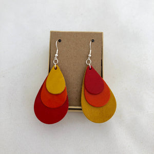 Tri Color Rainbow Earrings in Red Orange and Yellow. This pair of earrings features a mix-matched order of color, so one earring is yellow, orange, and red, whereas the other is red, orange and yellow. The earrings are pictured on a brown card in a brown jewelry box, which both come included with the earrings. They are pictured against a white background.