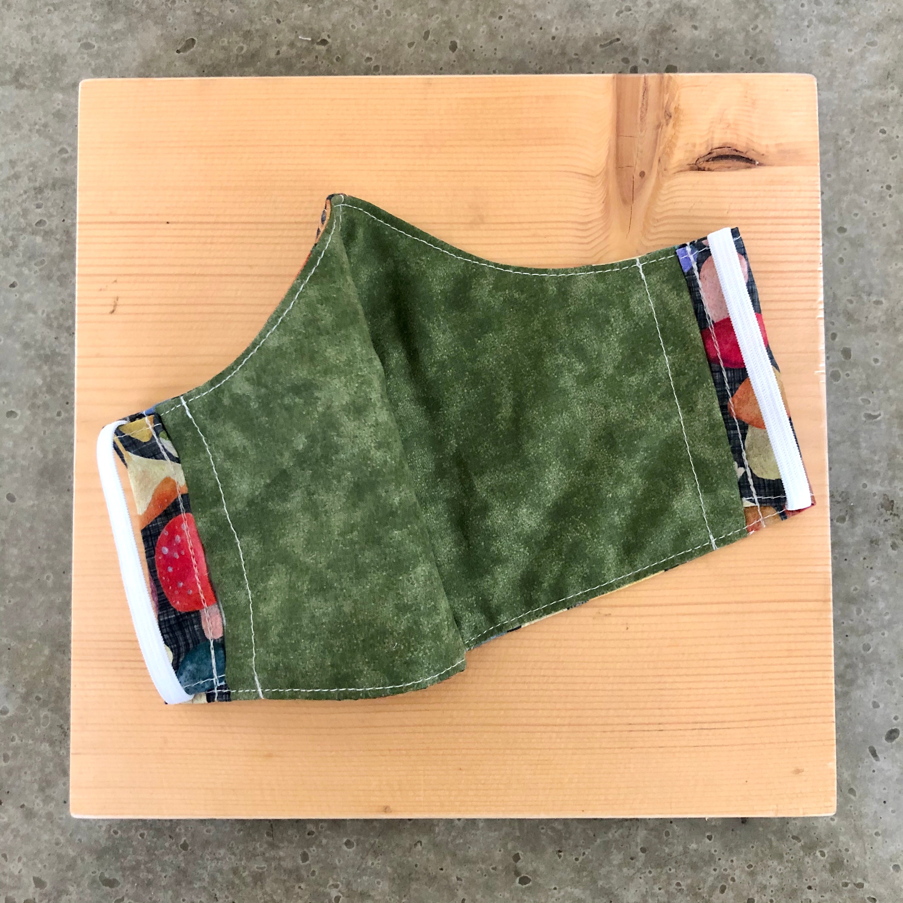 Inside view of the mushroom mask, showing the olive green fabric and ear elastic.