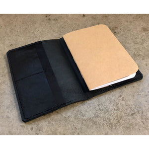All Black Leather Passport Wallet, pictured holding a small complimentary notebook made with recycled paper